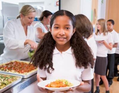 Female student in the lunch line holding her tray with kids behind her being served by the lunch staff.