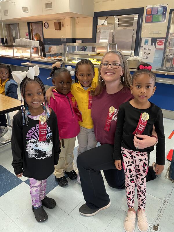 School Staff Woman poses for a picture with four small children.