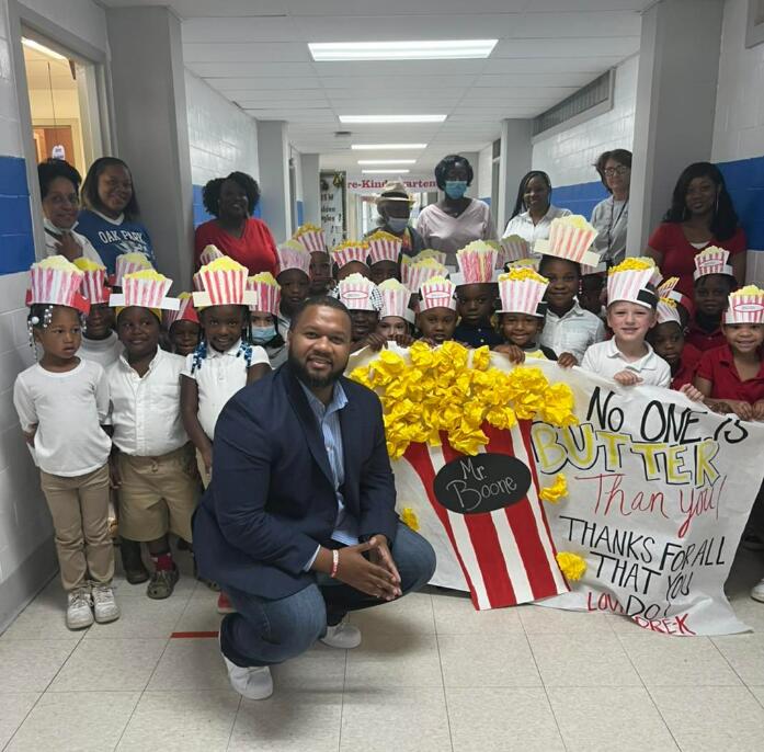 Male Principal posing with kids with a big popcorn sign